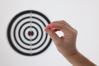 Photo of Targeting. Man with arrow aiming at dart board on light background, closeup