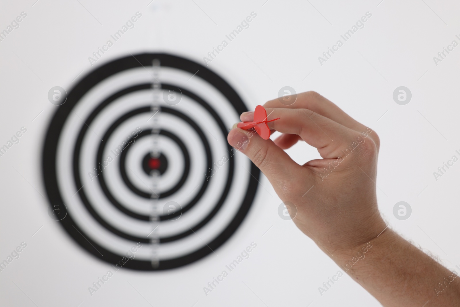 Photo of Targeting. Man with arrow aiming at dart board on light background, closeup