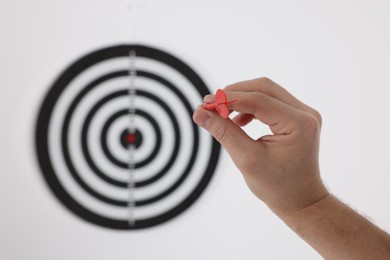 Photo of Targeting. Man with arrow aiming at dart board on light background, closeup