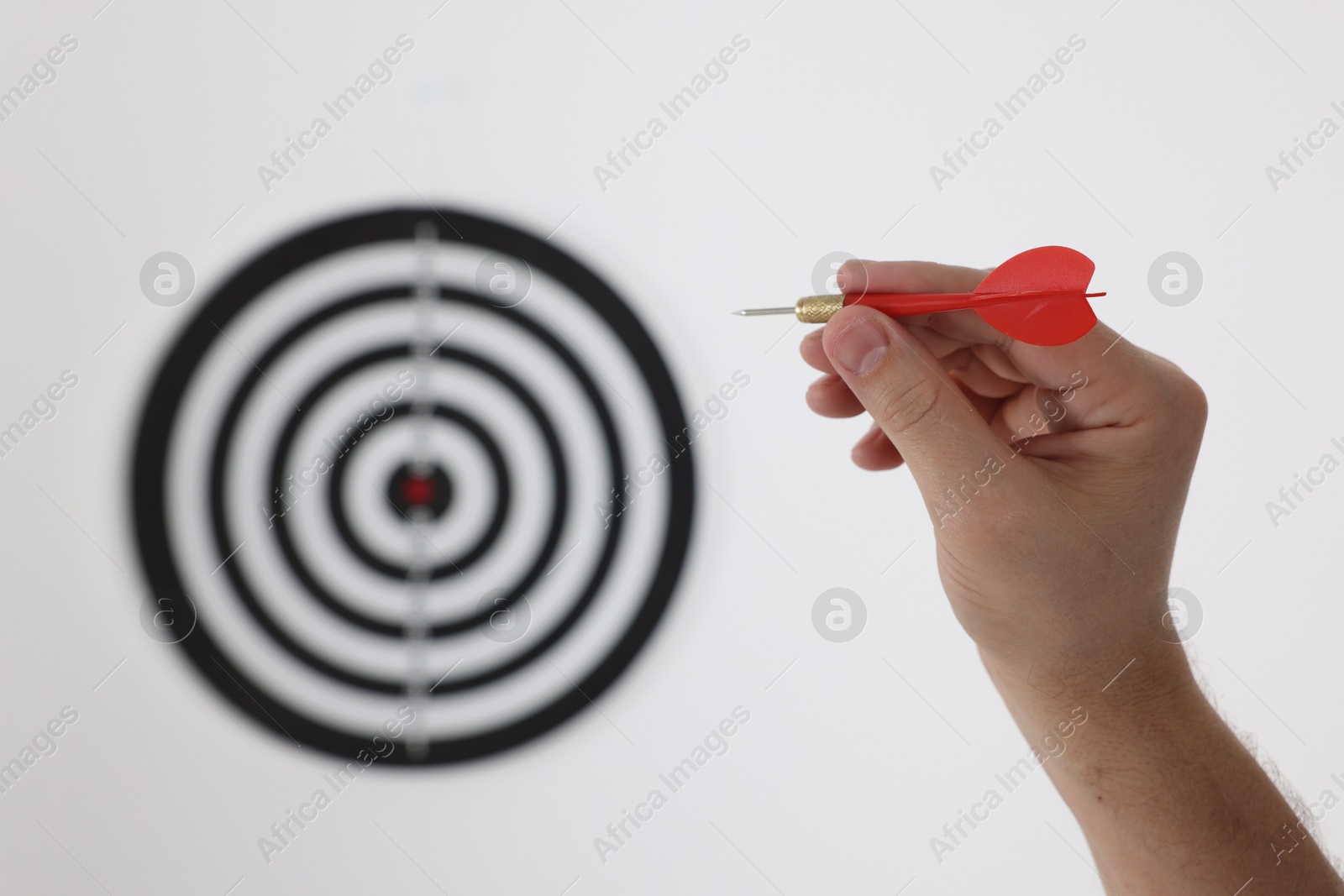 Photo of Targeting. Man with arrow aiming at dart board on light background, closeup