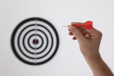 Photo of Targeting. Man with arrow aiming at dart board on light background, closeup