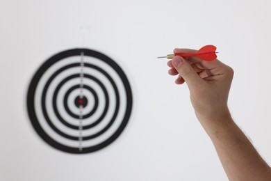Photo of Targeting. Man with arrow aiming at dart board on light background, closeup