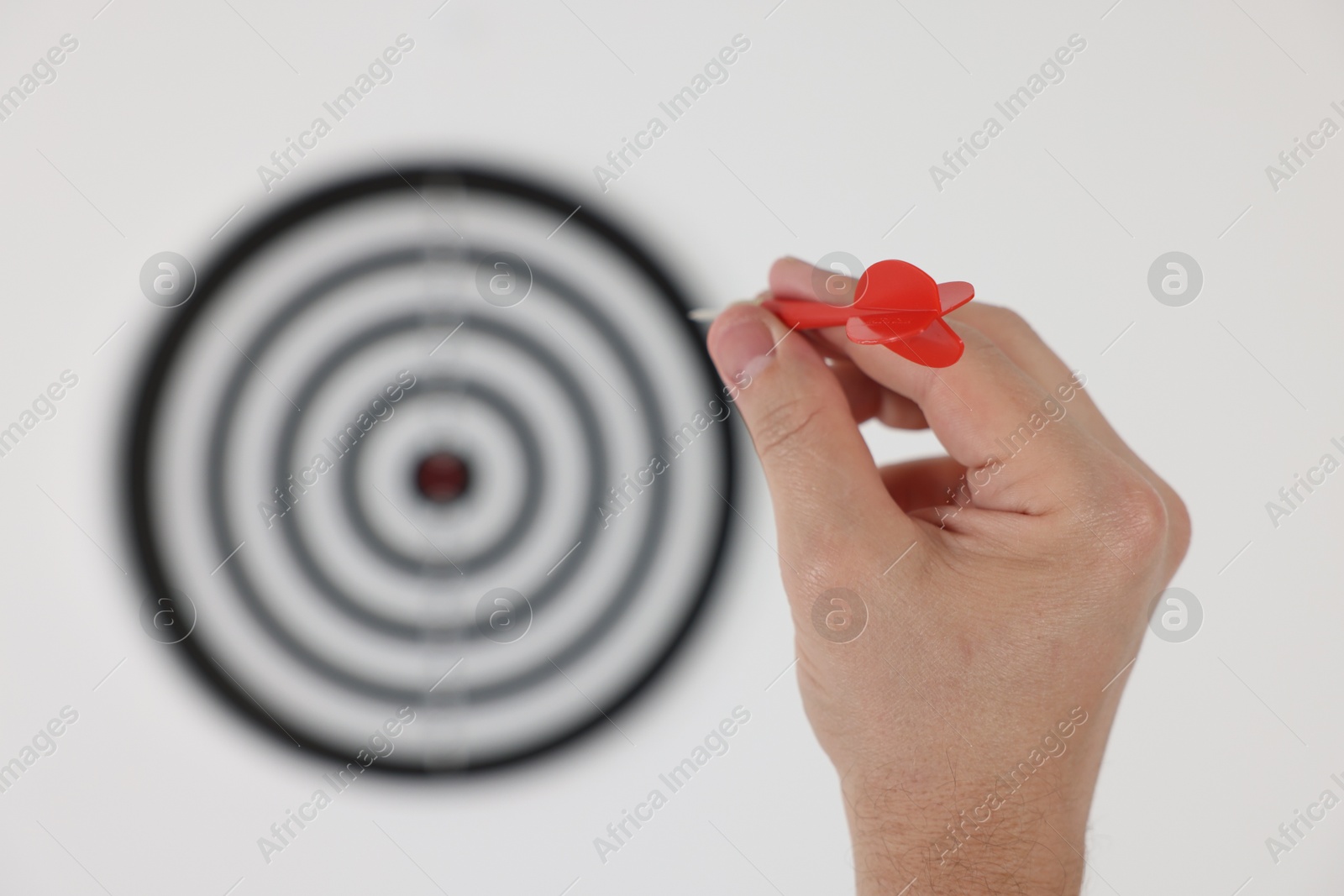 Photo of Targeting. Man with arrow aiming at dart board on light background, closeup