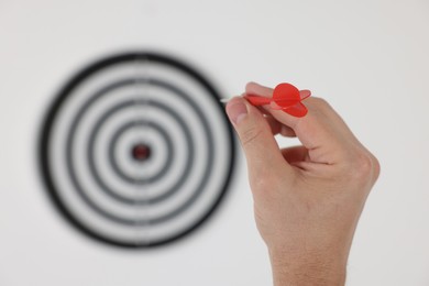 Photo of Targeting. Man with arrow aiming at dart board on light background, closeup