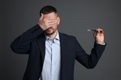 Photo of Targeting. Man with dart covering eyes on grey background
