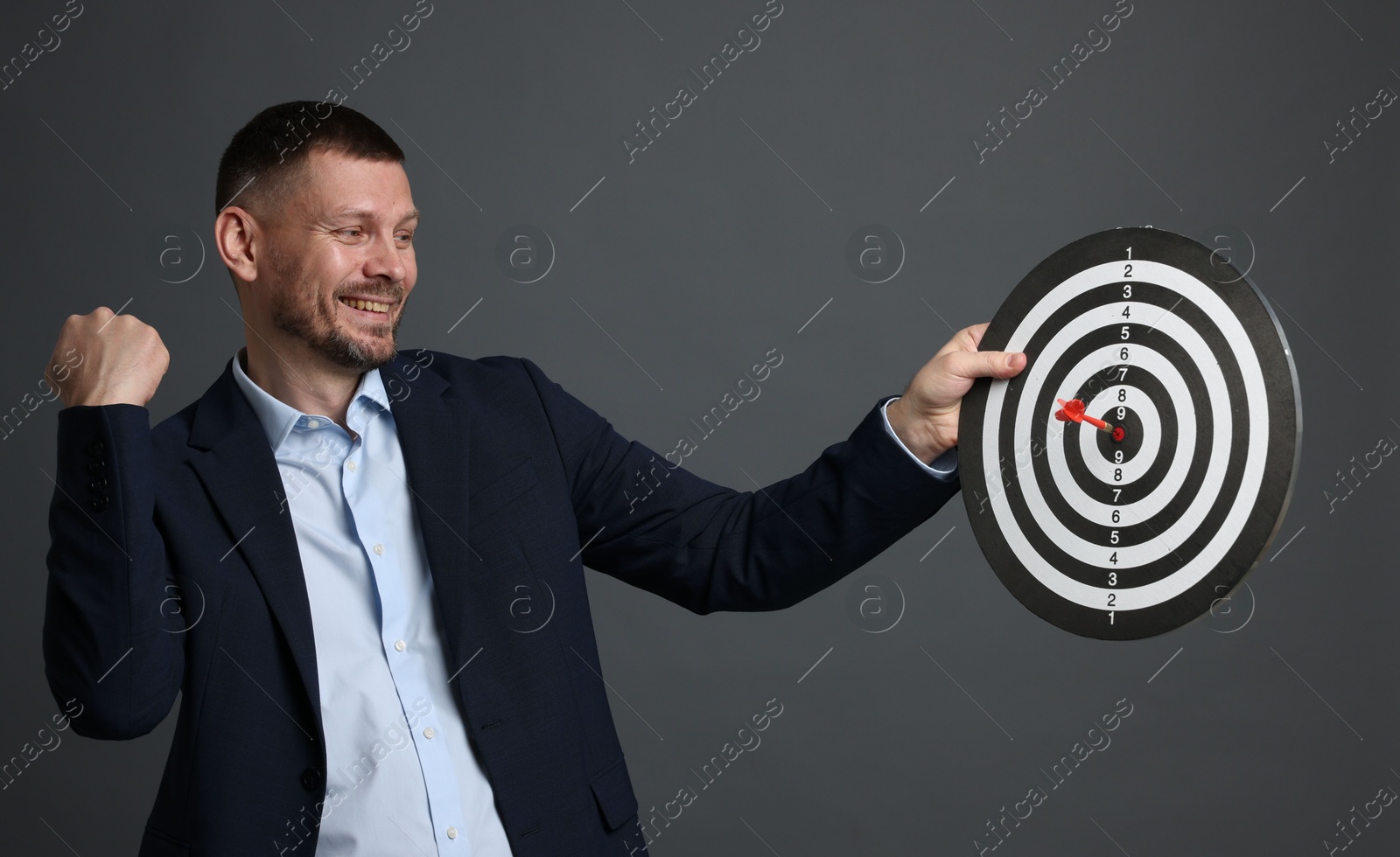 Targeting. Man with dart board and arrow on grey background Photo of Targeting. Man with dart board and arrow on grey background