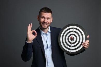 Photo of Targeting. Man with dart board and arrow showing ok gesture on grey background