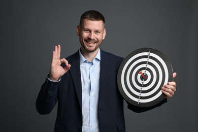 Photo of Targeting. Man with dart board and arrow showing ok gesture on grey background