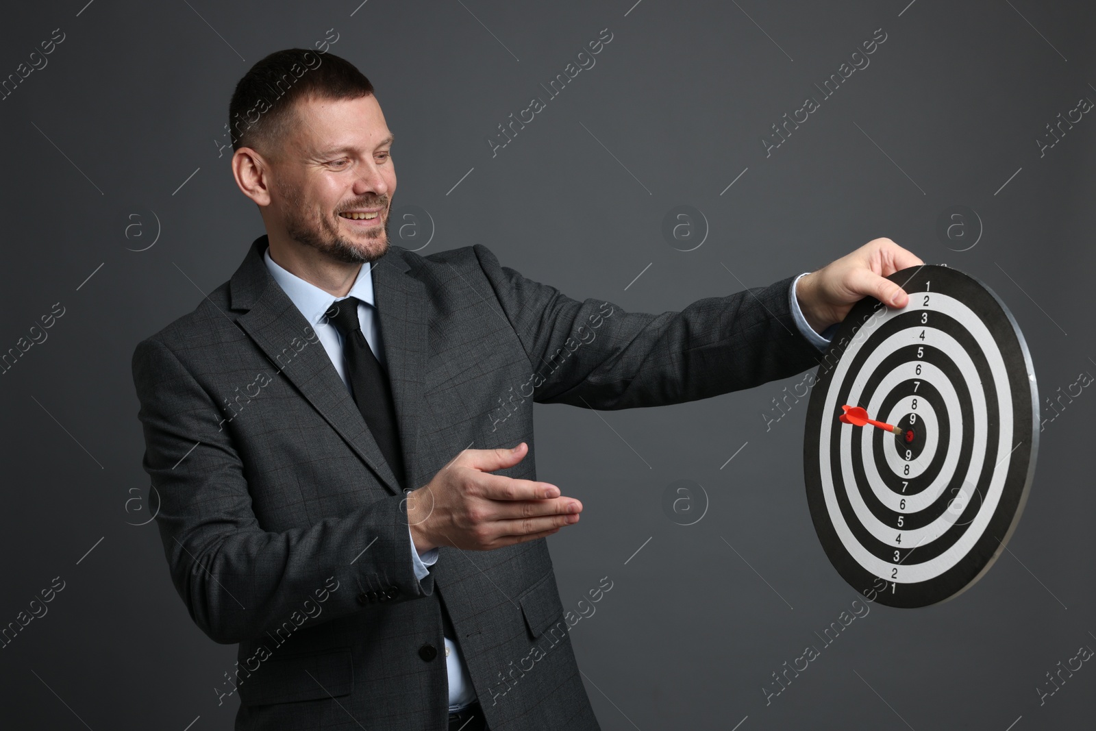 Targeting. Man with dart board and arrow on grey background Photo of Targeting. Man with dart board and arrow on grey background