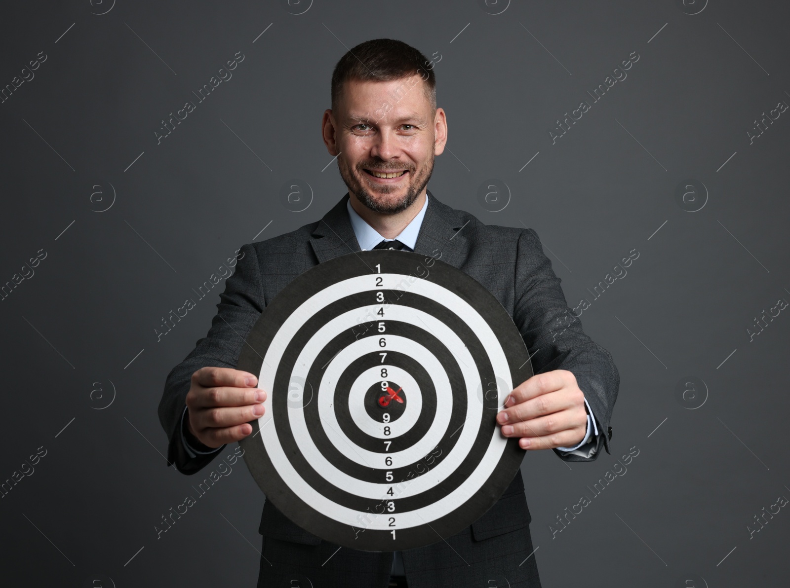 Targeting. Man with dart board and arrow on grey background Photo of Targeting. Man with dart board and arrow on grey background