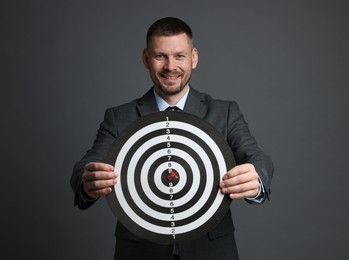 Photo of Targeting. Man with dart board and arrow on grey background