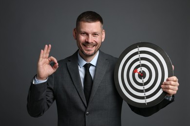 Photo of Targeting. Man with dart board and arrow showing ok gesture on grey background