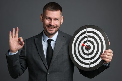 Photo of Targeting. Man with dart board and arrow showing ok gesture on grey background