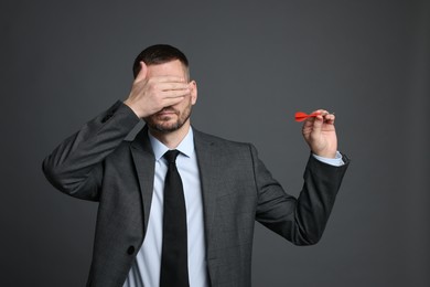 Photo of Targeting. Man with dart covering eyes on grey background