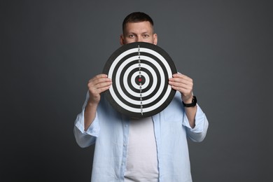 Photo of Targeting. Man with dart board on grey background