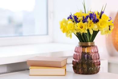 Photo of Bouquet of beautiful flowers in vase and books on desk near window indoors