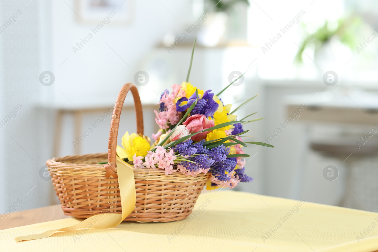 Wicker basket with beautiful flowers on table indoors Photo of Wicker basket with beautiful flowers on table indoors