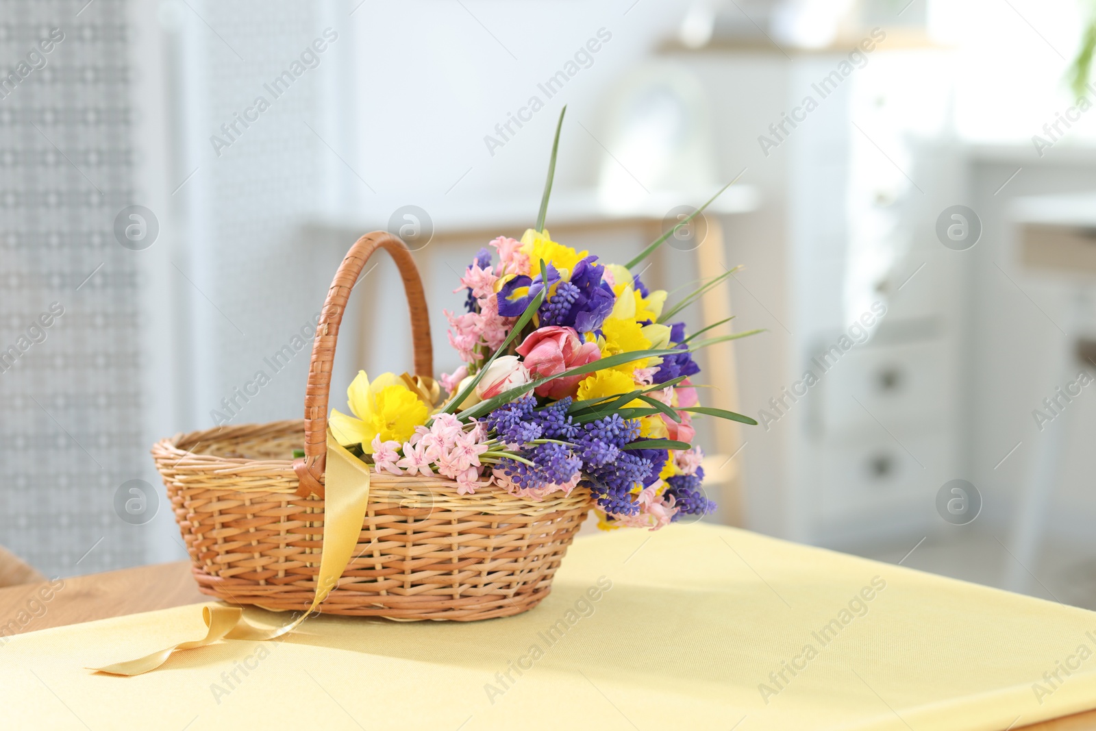 Wicker basket with beautiful flowers on table indoors Photo of Wicker basket with beautiful flowers on table indoors