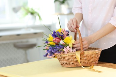 Photo of Woman and wicker basket with beautiful flowers at table indoors, closeup. Space for text