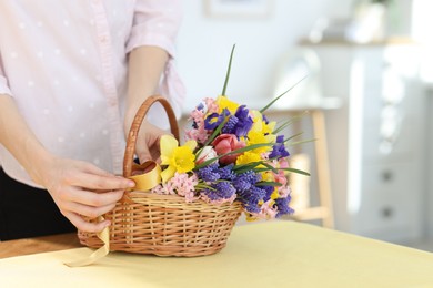 Photo of Woman and wicker basket with beautiful flowers at table indoors, closeup