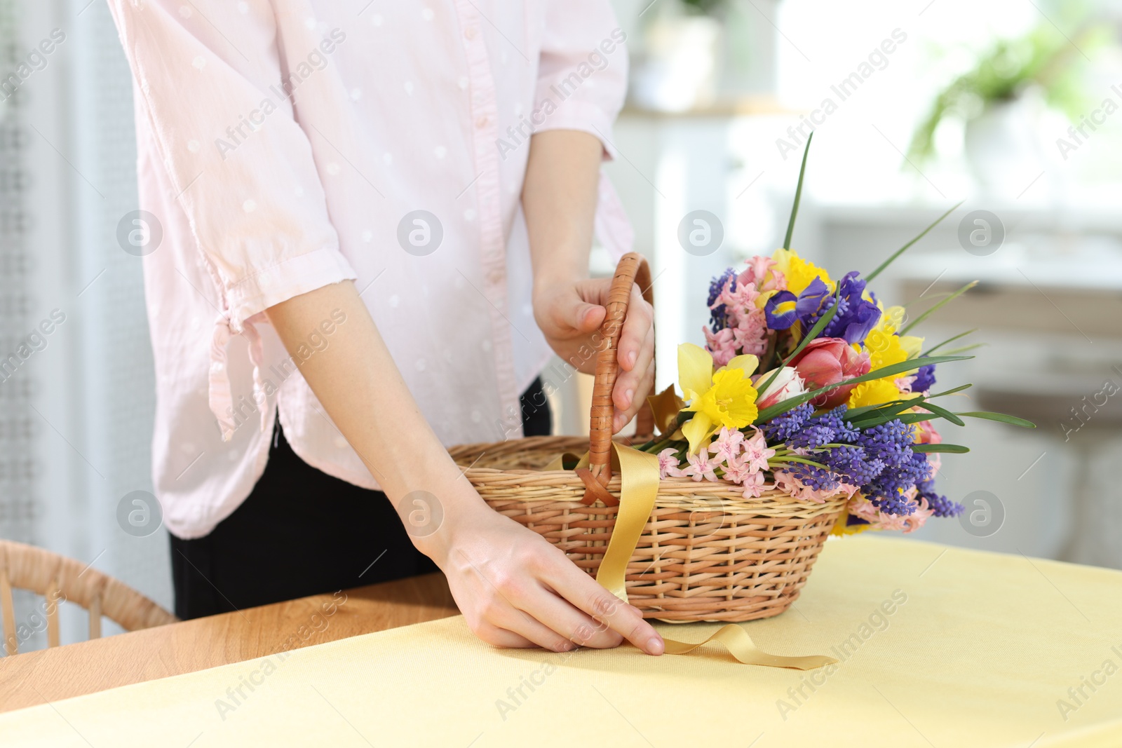 Woman and wicker basket with beautiful flowers at table indoors, closeup Photo of Woman and wicker basket with beautiful flowers at table indoors, closeup