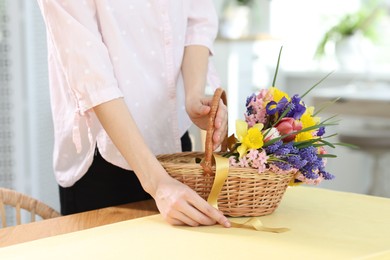 Photo of Woman and wicker basket with beautiful flowers at table indoors, closeup