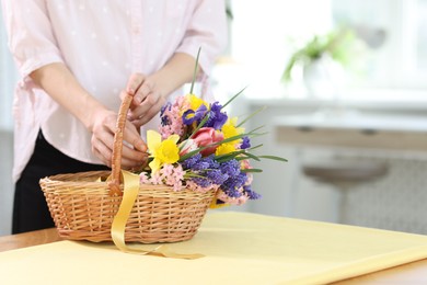 Photo of Woman and wicker basket with beautiful flowers at table indoors, closeup. Space for text