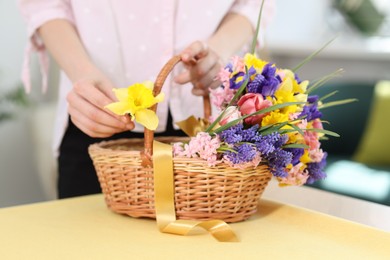Photo of Woman and wicker basket with beautiful flowers at table indoors, closeup