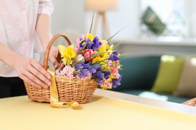 Photo of Woman and wicker basket with beautiful flowers at table indoors, closeup