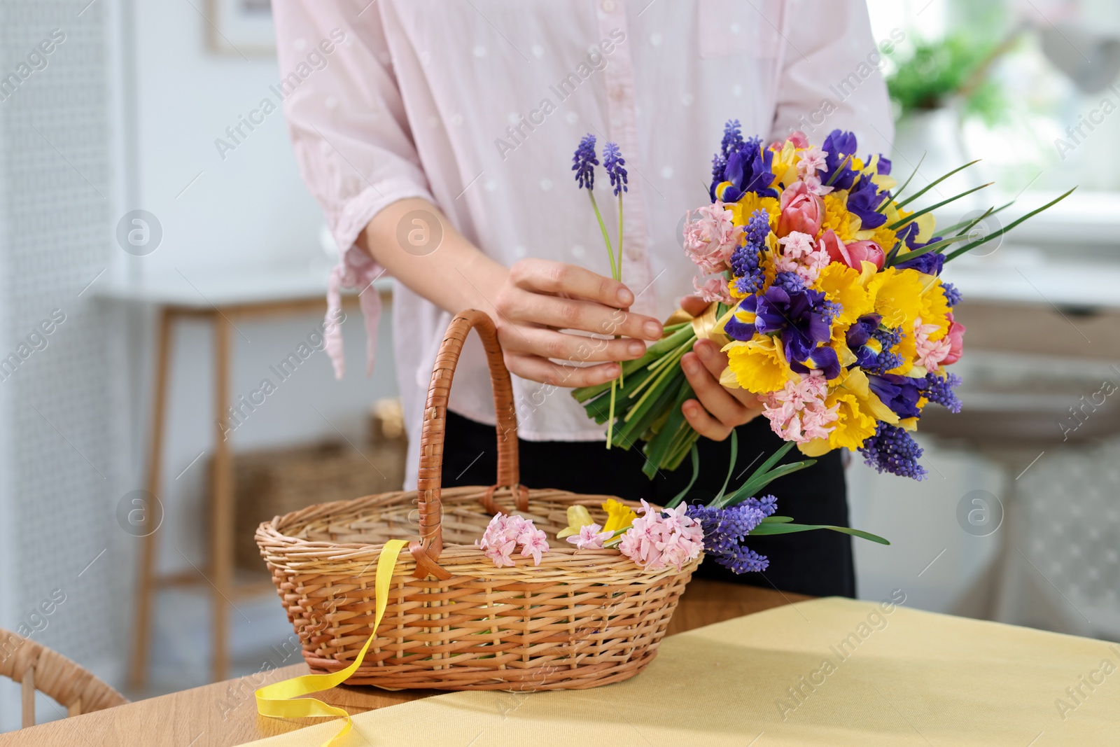Woman with bouquet of beautiful flowers and wicker basket at table indoors, closeup Photo of Woman with bouquet of beautiful flowers and wicker basket at table indoors, closeup