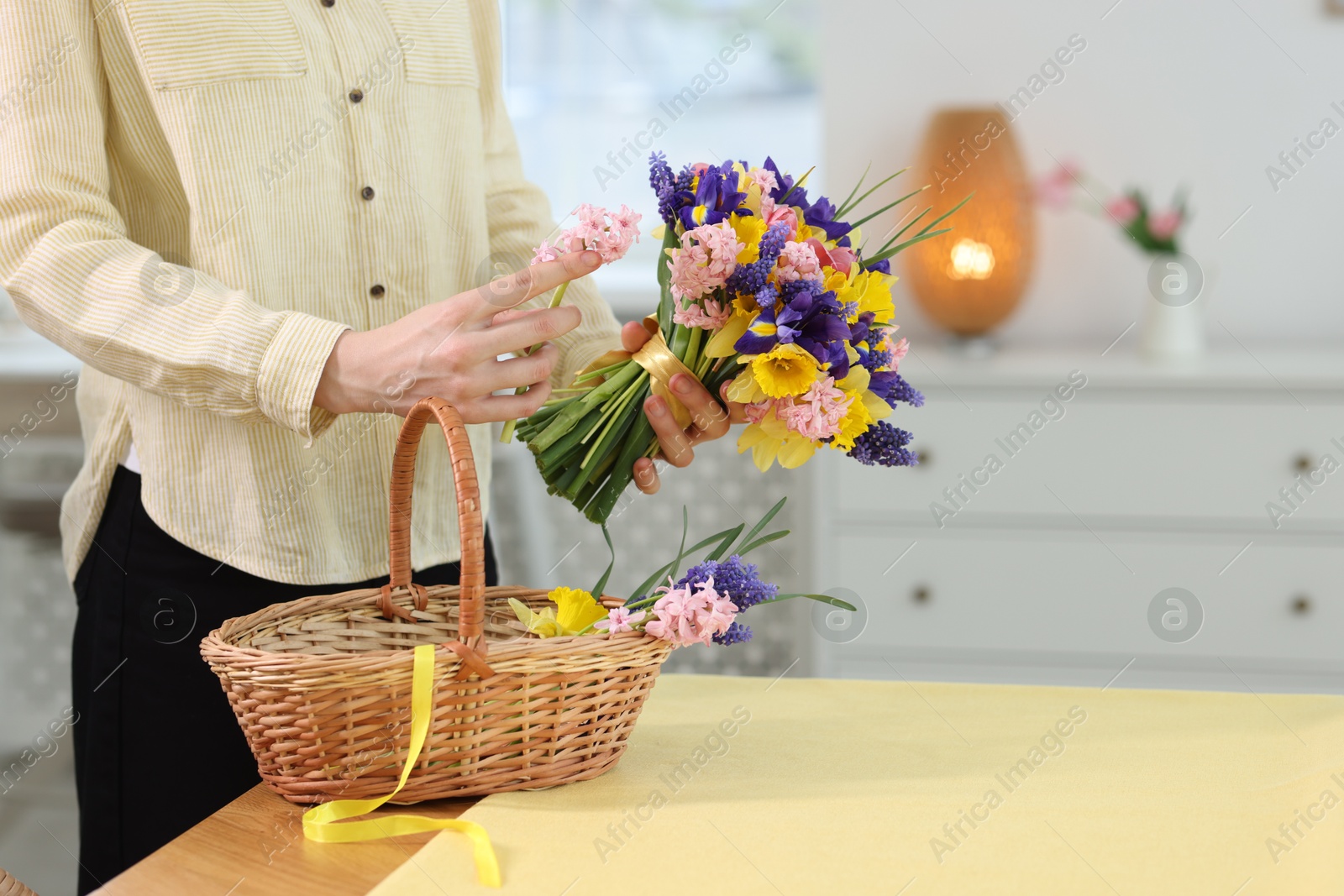 Woman with bouquet of beautiful flowers and wicker basket at table indoors, closeup Photo of Woman with bouquet of beautiful flowers and wicker basket at table indoors, closeup