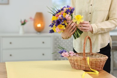 Photo of Woman with bouquet of beautiful flowers and wicker basket at table indoors, closeup. Space for text
