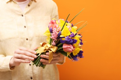 Photo of Woman with bouquet of beautiful flowers on orange background, closeup. Space for text
