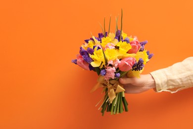 Photo of Woman with bouquet of beautiful flowers on orange background, closeup. Space for text