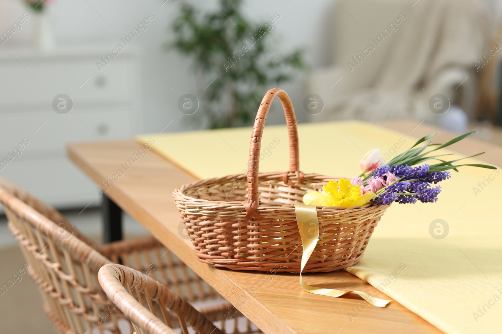 Wicker basket with beautiful flowers on table indoors Photo of Wicker basket with beautiful flowers on table indoors