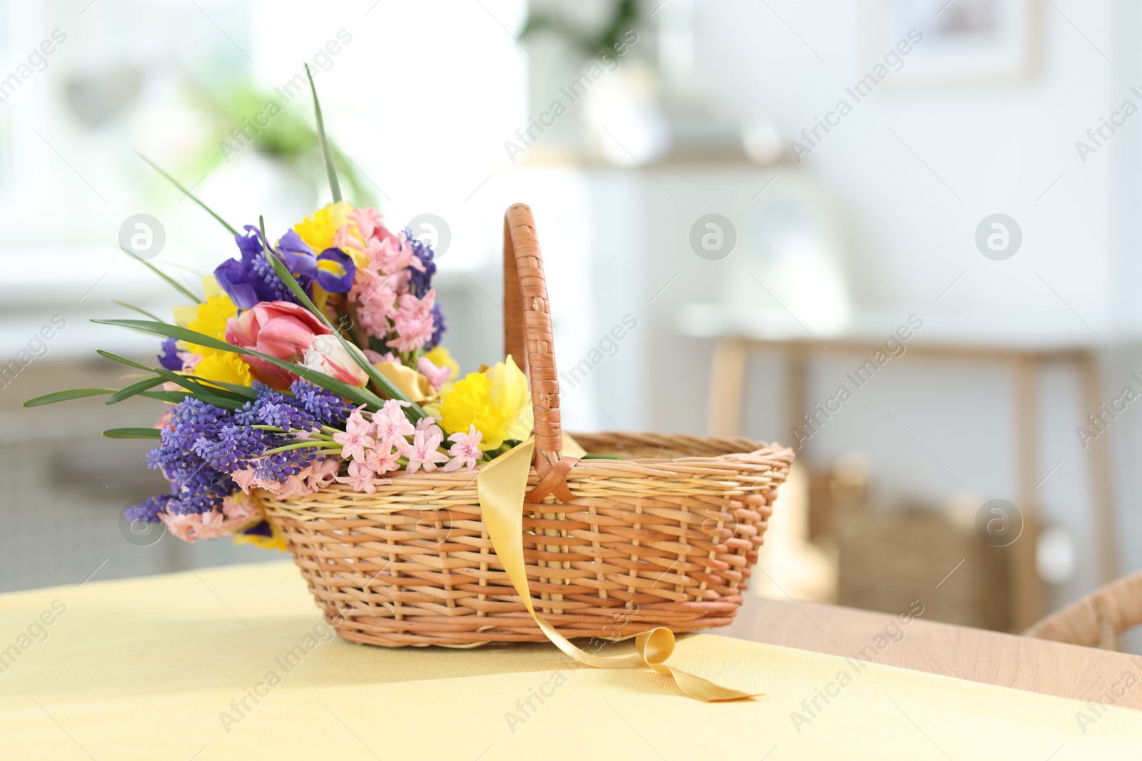 Wicker basket with beautiful flowers on table indoors Photo of Wicker basket with beautiful flowers on table indoors
