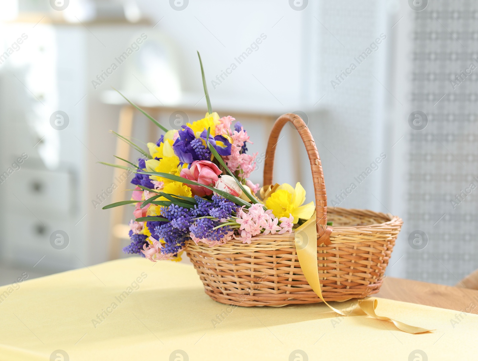 Wicker basket with beautiful flowers on table indoors Photo of Wicker basket with beautiful flowers on table indoors