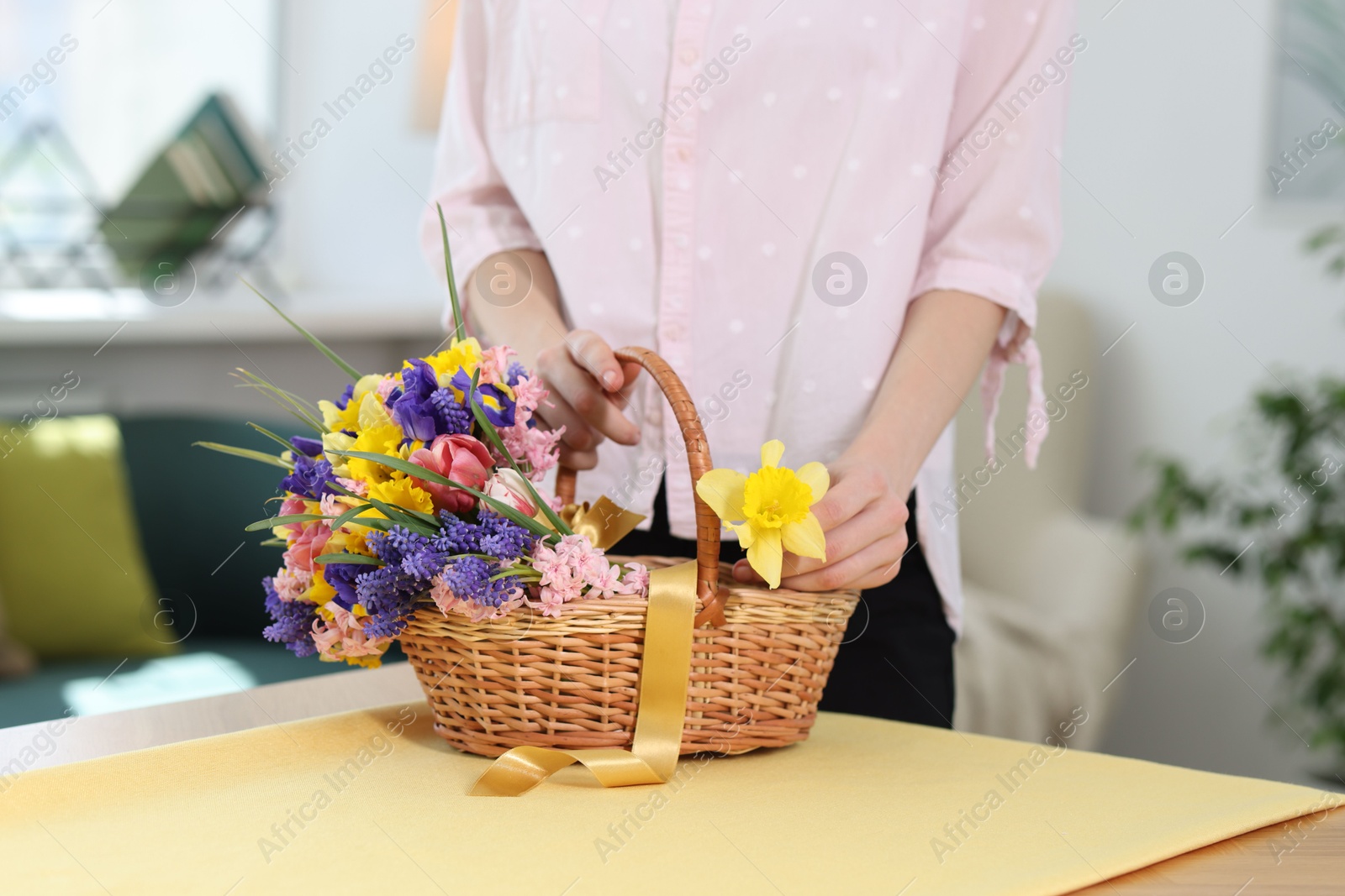 Woman and wicker basket with beautiful flowers at table indoors, closeup Photo of Woman and wicker basket with beautiful flowers at table indoors, closeup