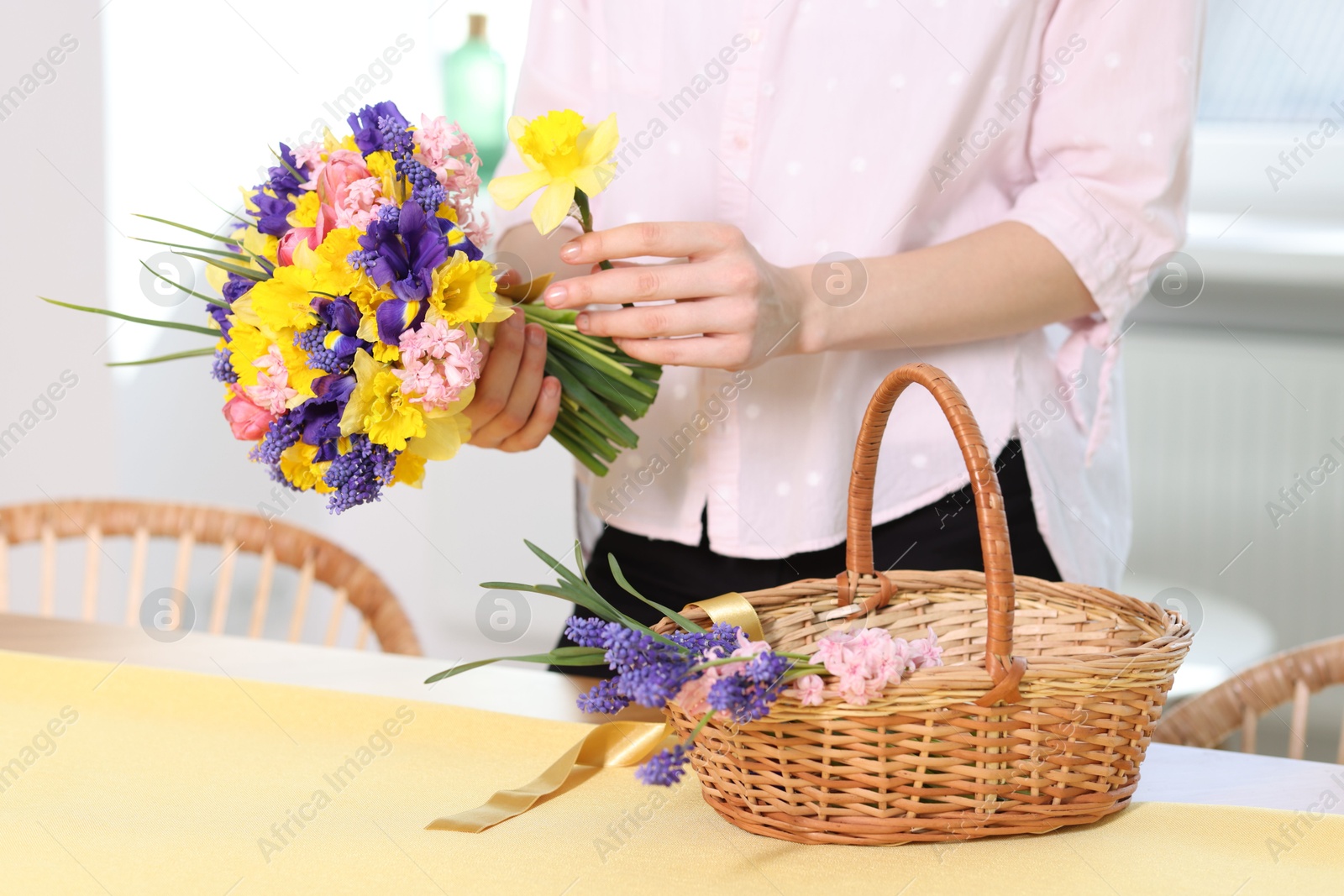 Woman with bouquet of beautiful flowers and wicker basket at table indoors, closeup Photo of Woman with bouquet of beautiful flowers and wicker basket at table indoors, closeup