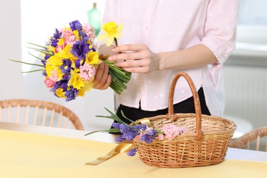 Photo of Woman with bouquet of beautiful flowers and wicker basket at table indoors, closeup