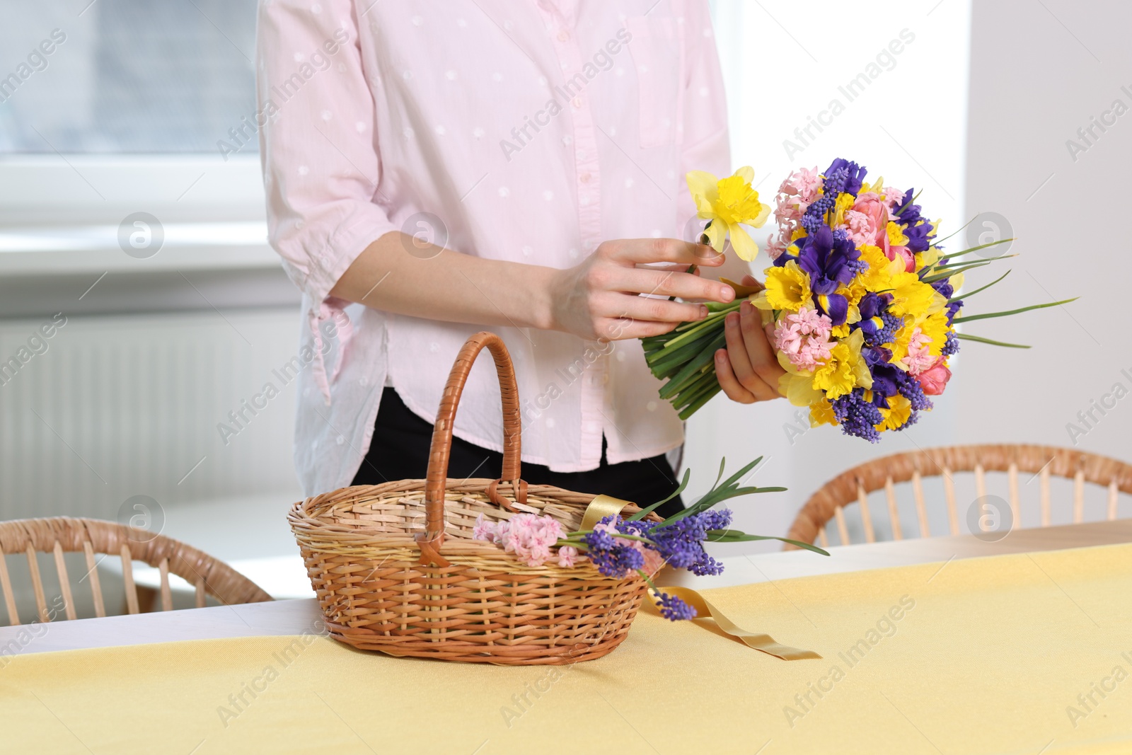 Woman with bouquet of beautiful flowers and wicker basket at table indoors, closeup Photo of Woman with bouquet of beautiful flowers and wicker basket at table indoors, closeup