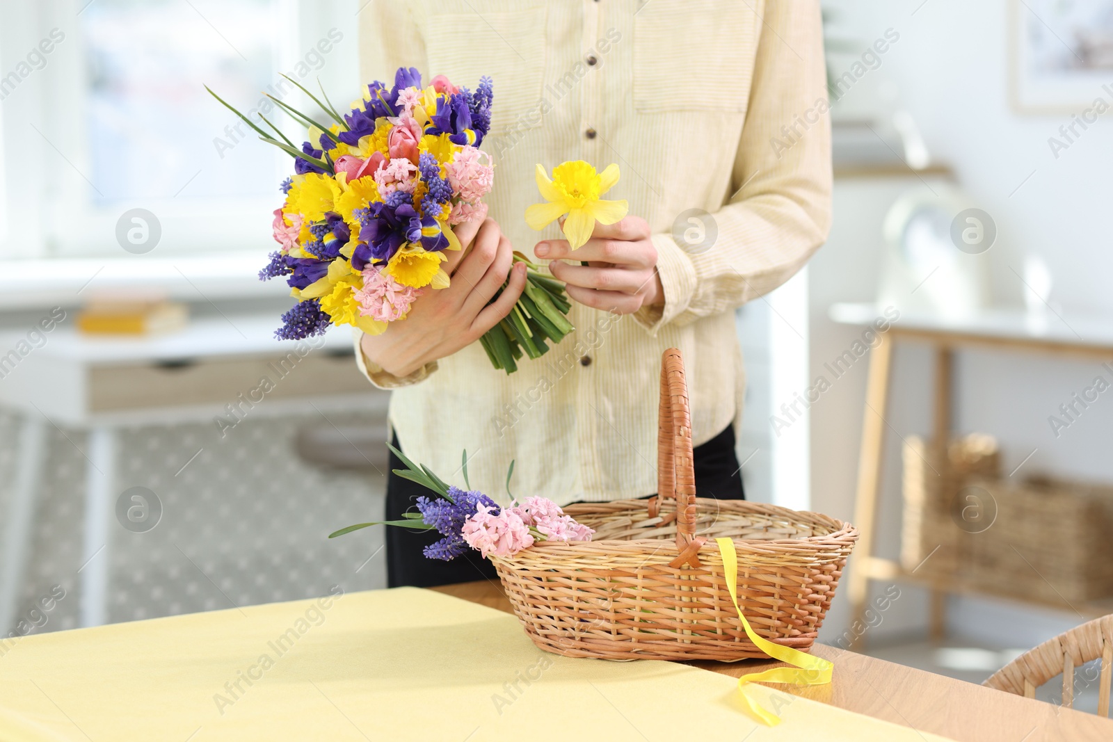 Woman with bouquet of beautiful flowers and wicker basket at table indoors, closeup Photo of Woman with bouquet of beautiful flowers and wicker basket at table indoors, closeup