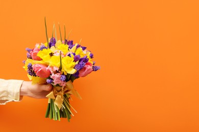 Photo of Woman with bouquet of beautiful flowers on orange background, closeup. Space for text
