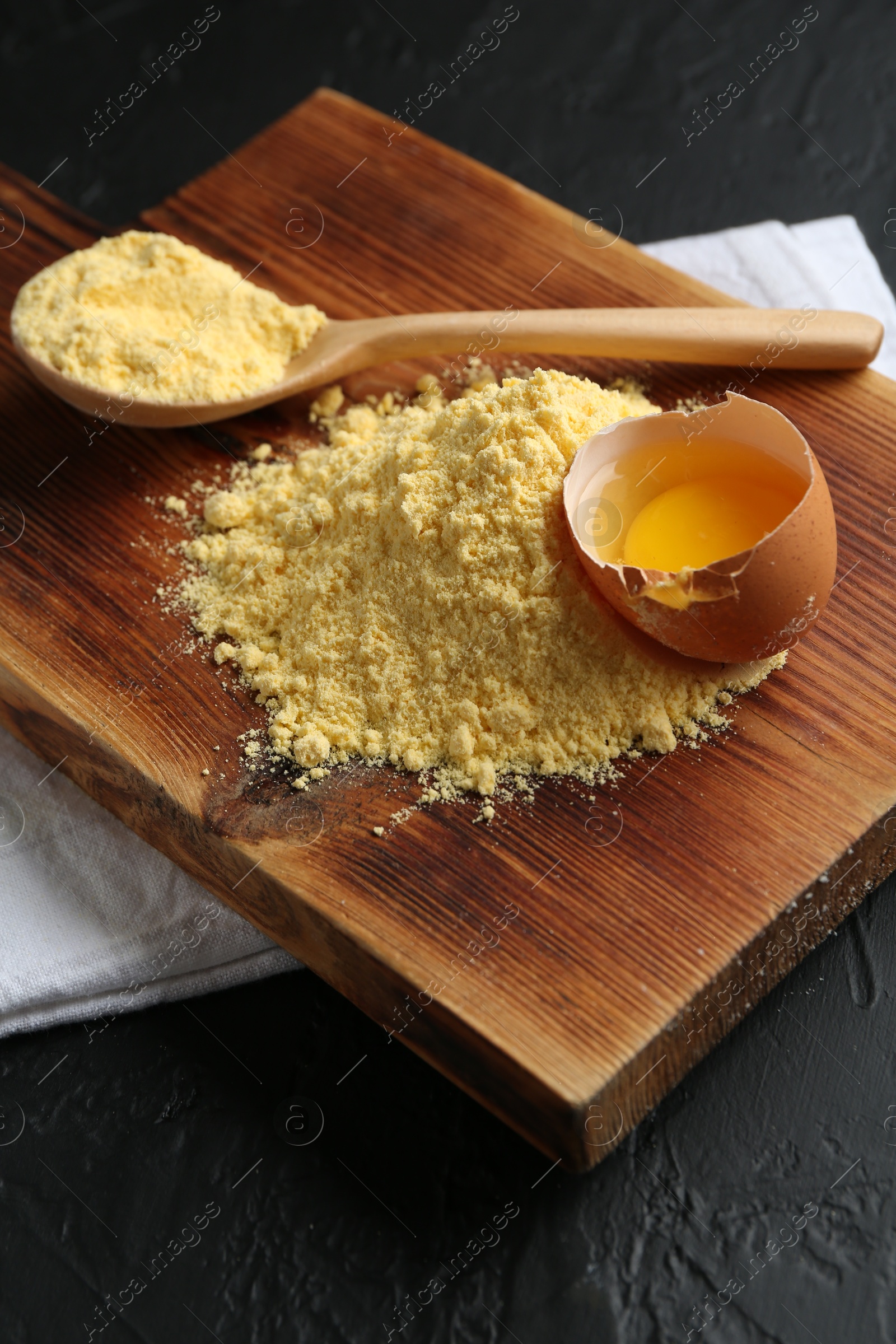 Pile of corn flour, spoon and broken egg on black textured table, closeup Photo of Pile of corn flour, spoon and broken egg on black textured table, closeup
