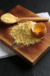 Photo of Pile of corn flour, spoon and broken egg on black textured table, closeup