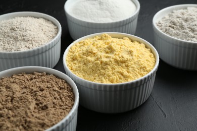 Photo of Different types of flour in bowls on black textured table, closeup