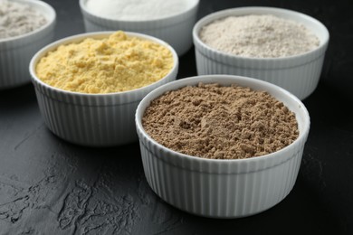 Photo of Different types of flour in bowls on black textured table, closeup