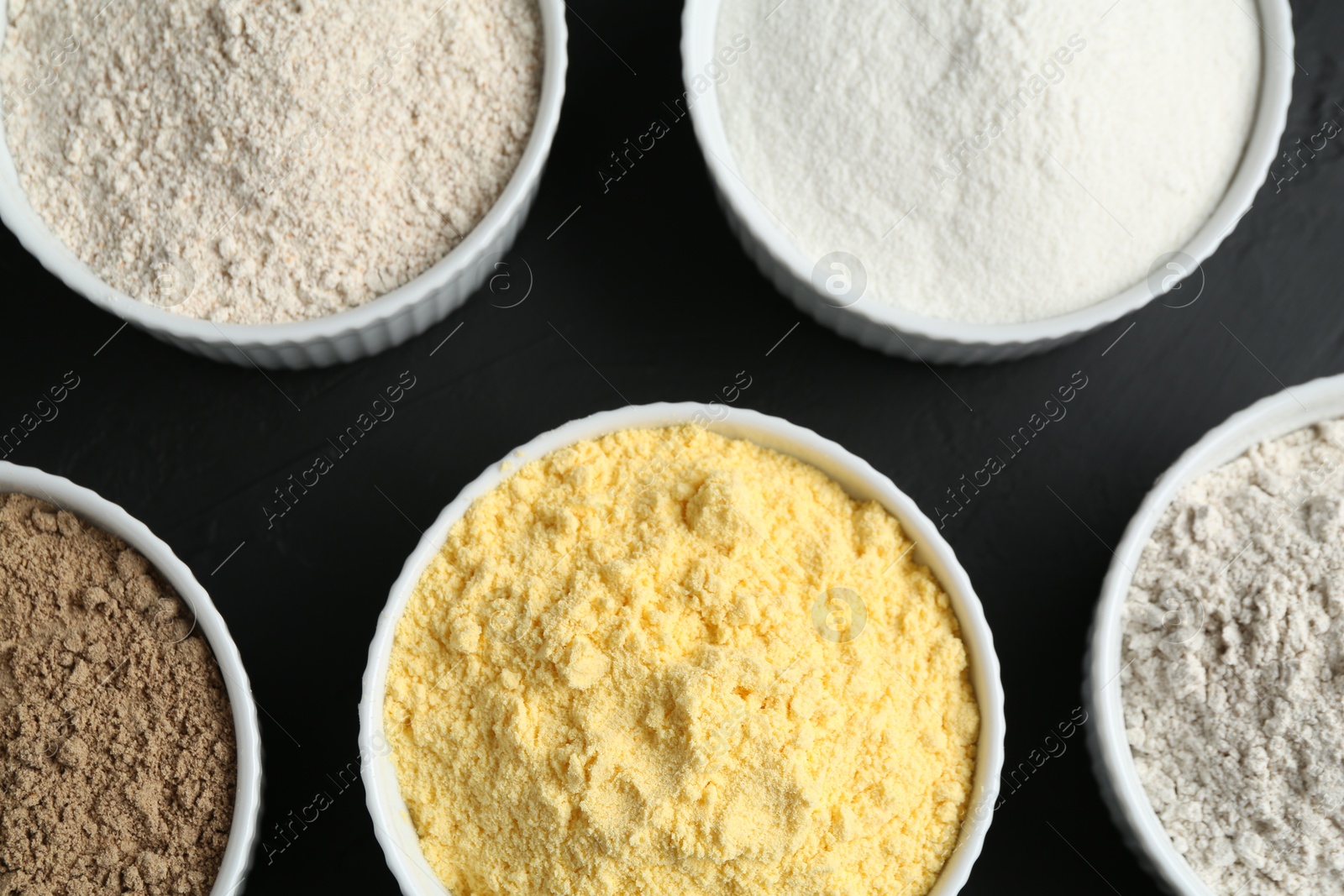 Different types of flour in bowls on black table, flat lay Photo of Different types of flour in bowls on black table, flat lay