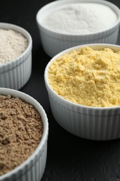 Photo of Different types of flour in bowls on black table, closeup