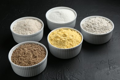 Photo of Different types of flour in bowls on black textured table, closeup
